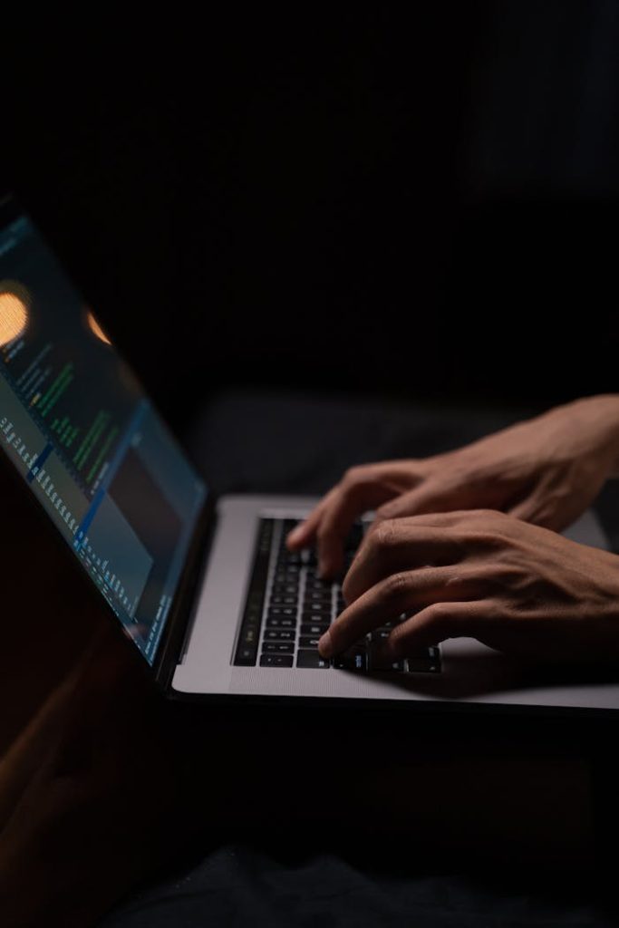 Hands typing code on a laptop keyboard in a dark room, capturing the essence of late-night programming.